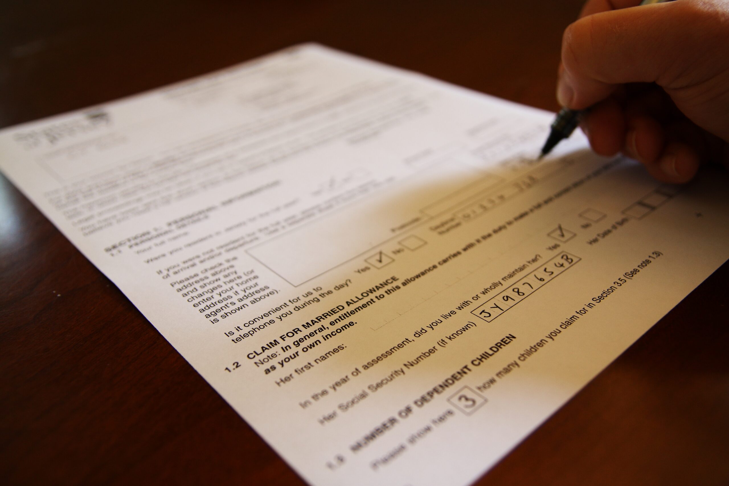 hand-with-pen-filling-in-a-form-on-desk-2022-11-02-17-37-10-utc